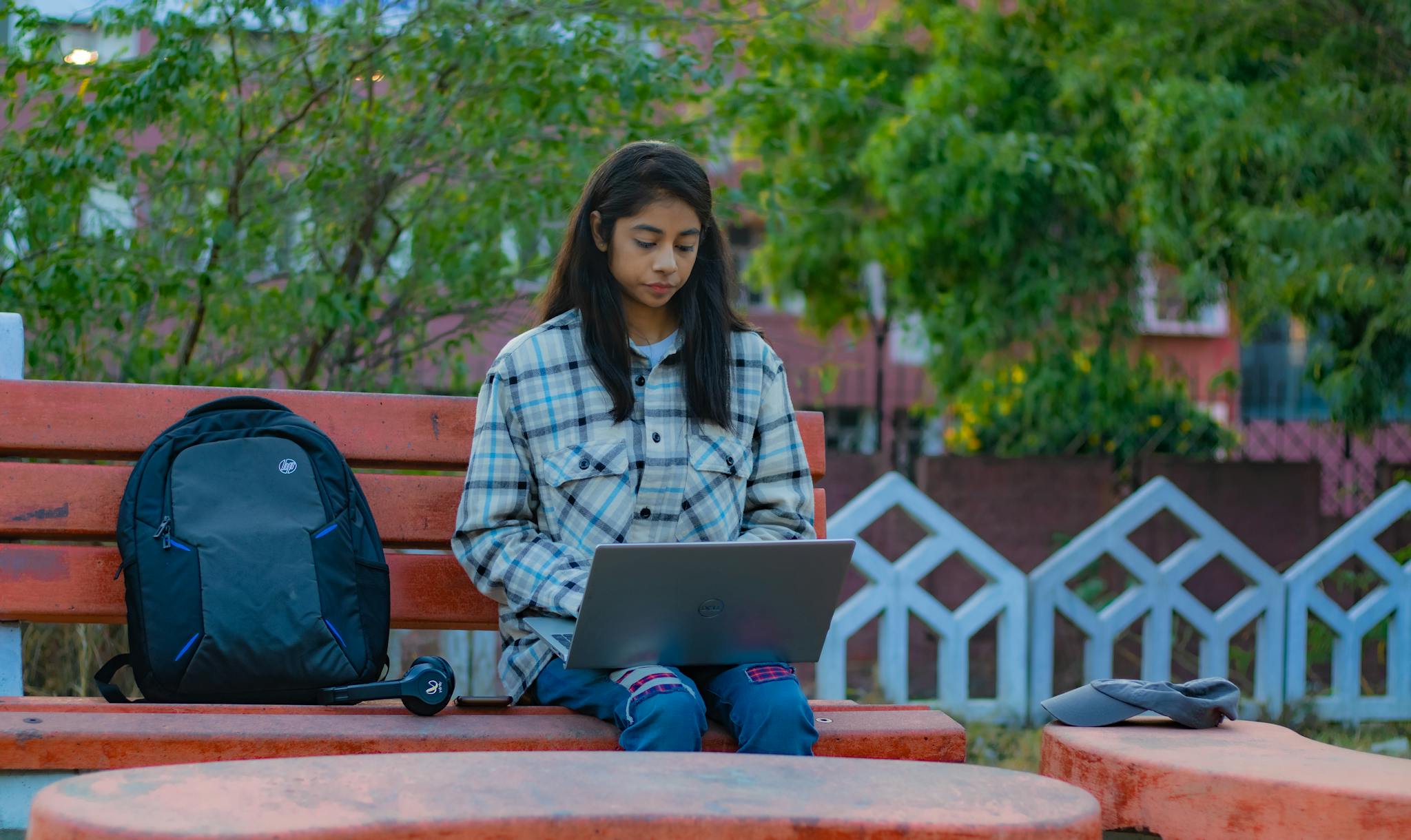 A young woman using a laptop on a park bench in Greater Noida.