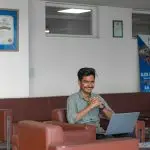 Smiling young adult sitting with laptop in a modern office lounge, focusing on work.